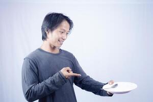 asian man pointing towards empty plate with happy expression isolated white background for coffee photo space. food menu presentation concept.