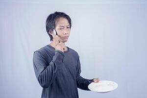 handsome asian man holding empty plate while thinking for serving food menu on isolated white background for advertising menu. menu presentation concept. photo