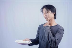 handsome asian man holding empty plate while thinking for serving food menu on isolated white background for advertising menu. menu presentation concept. photo