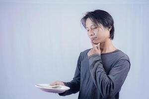 handsome asian man holding empty plate while thinking for serving food menu on isolated white background for advertising menu. menu presentation concept. photo