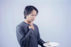 handsome asian man holding empty plate while thinking for serving food menu on isolated white background for advertising menu. menu presentation concept. photo