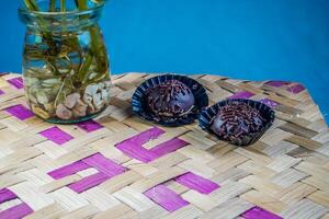 Isolated chocolate dumplings, close-up view of chocolate dumplings sprinkled with sprinkles, with woven bamboo as a base and ornamental plants on the side. Eid meal concept. photo