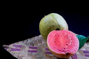 Guava isolated. Collection of red fleshed guava fruit with yellowish green skin and leaves isolated on black background with woven bamboo. photo