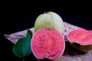 Guava isolated. Collection of red fleshed guava fruit with yellowish green skin and leaves isolated on black background with woven bamboo. photo