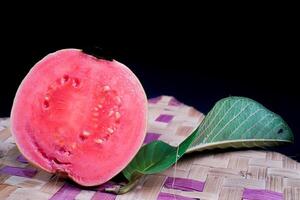 Guava isolated. Guava fruit with red flesh with yellowish green skin and leaves isolated on a black background with woven bamboo as a base. photo