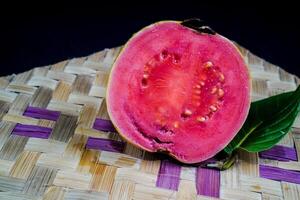 Guava isolated. Guava fruit with red flesh with yellowish green skin and leaves isolated on a black background with woven bamboo as a base. photo