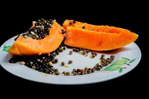 close up view of papaya fruit isolated on plate on black background. photo