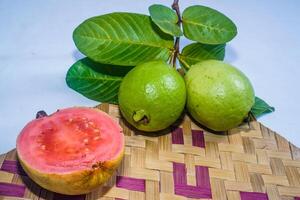 Guava isolated. Collection of red fleshed guava fruit with yellowish green skin and leaves isolated on a white background with bamboo matting. photo