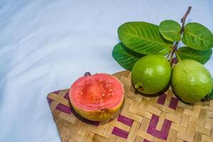 Guava isolated. Collection of red fleshed guava fruit with yellowish green skin and leaves isolated on a white background with bamboo matting. photo