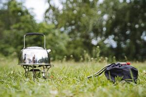 Iron kettle stands on the fire of a tourist burner, boil water on a hike, camping equipment, dishes for relaxation, steam from the spout of the kettle photo