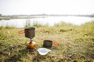 Camping in nature by the river, the concept of a tourist kitchen on a hike, a set of plates with handles, dishes for cooking on a gas burner on a hike. photo