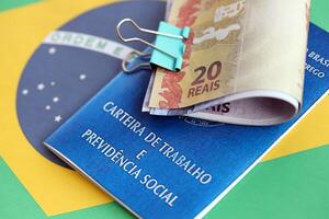 Brazilian work card and social security blue book and reais money bills on flag of Federative Republic of Brazil photo