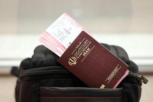 Red Islamic Republic of Iran passport with airline tickets on touristic backpack photo