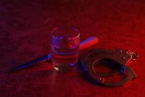 Glass with vodka alcohol drink, knife and handcuffs. Concept of alcoholism, criminal photo