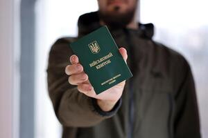 Young ukrainian conscript soldier shows his military token or army ID ticket indoors photo