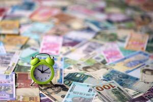 Small alarm clock on many banknotes of different currency. Background of time and money photo