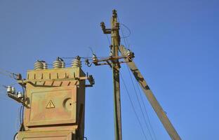 Old and obsolete electrical transformer against the background of a cloudless blue sky. Device for distribution of supply of high-voltage energy photo