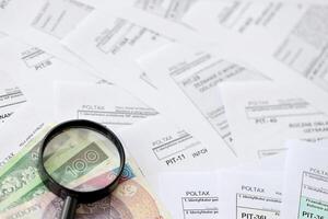 Polish zloty money and magnifying glass on big amount of polish tax forms close up. Accounting, bureaucracy and taxpayers routine photo