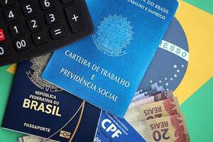 Passport of Brazil, CPF taxpayer card and work card with brazilian reais money bills on flag photo