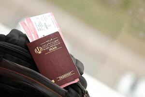 Red Islamic Republic of Iran passport with airline tickets on touristic backpack photo