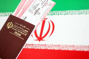Red Islamic Republic of Iran passport with airline tickets on Iranian flag background close up photo