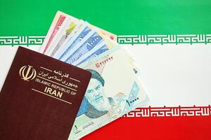 Red Islamic Republic of Iran passport and iranian reals money bills background close up photo