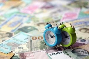 Small alarm clock on many banknotes of different currency. Background of time and money photo