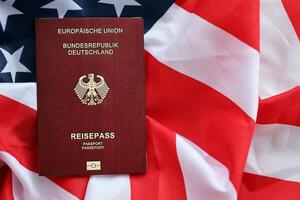 Red German passport of European Union on United States national flag background close up photo