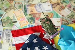 Toy tank on US flag and ukrainian flag on many banknotes of different currency photo