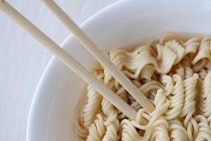Bowl of instant cooking noodles with wooden chopsticks on white wooden table photo