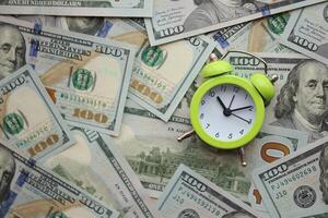 Alarm clock on hundred dollar bills banknotes. Background of time management, business photo