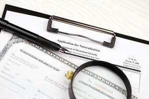 N-400 Application for Naturalization and Certificate of naturalization on A4 tablet lies on office table with pen and magnifying glass photo