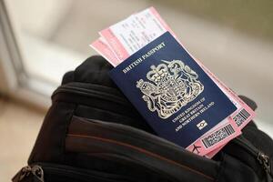 Blue British passport with airline tickets on touristic backpack photo