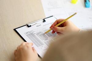 Female student hands testing in exercise and taking fill in exam paper sheet with pencil at school test photo