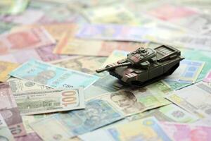 Small green tank on many banknotes of different currency. Background of war funding photo