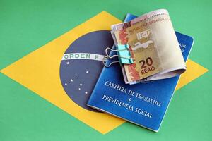 Brazilian work card and social security blue book and reais money bills on flag of Federative Republic of Brazil photo