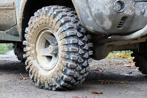 Wheel closeup in a countryside landscape with a mud road. Off-road 4x4 suv automobile with ditry body after drive in muddy road photo