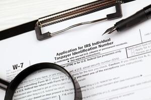 IRS Form W-7 Application for IRS Individual taxpayer identification number blank on A4 tablet lies on office table with pen and magnifying glass photo