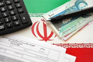 Iranian annual income tax return form F20-25-006 ready to fill on table with pen, calculator and iranian money on flag photo