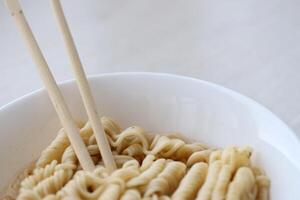 Bowl of instant cooking noodles with wooden chopsticks on white wooden table photo