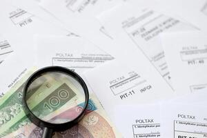 Polish zloty money and magnifying glass on big amount of polish tax forms close up. Accounting, bureaucracy and taxpayers routine photo