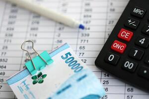 Business calculations with indonesian rupiah money bills and calculator with pen on office table photo