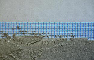 The texture of the wall, covered with gray foam polystyrene plates, covered with a blue reinforcing mesh and covered with a mixture for gluing it. Stage of wall insulation photo