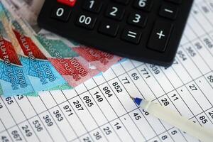 Business calculations with indonesian rupiah money bills and calculator with pen on office table photo