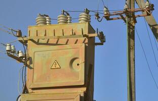 Old and obsolete electrical transformer against the background of a cloudless blue sky. Device for distribution of supply of high-voltage energy photo