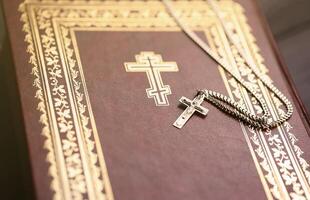 Silver necklace with crucifix cross on christian holy bible book on black wooden table. Asking blessings from God with the power of holiness, which brings luck photo