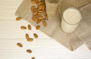 vaso de leche de almendras con nueces de almendras sobre tela de lona sobre mesa de madera blanca. leche alternativa láctea para desintoxicación, alimentación saludable y dietas foto