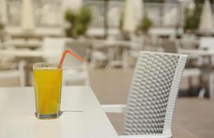 Glass of orange juice with plastic straw on white table in restaurant outdoor lounge zone photo