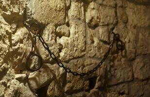 Slavery and bondage strong steel old shackles on stone wall in castle cellar photo