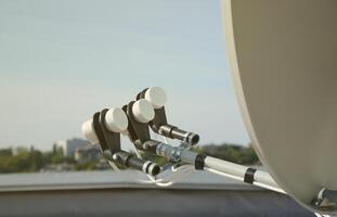 White satellite dish with three converters mounted on residental building rooftop concrete wall. Satellite television photo